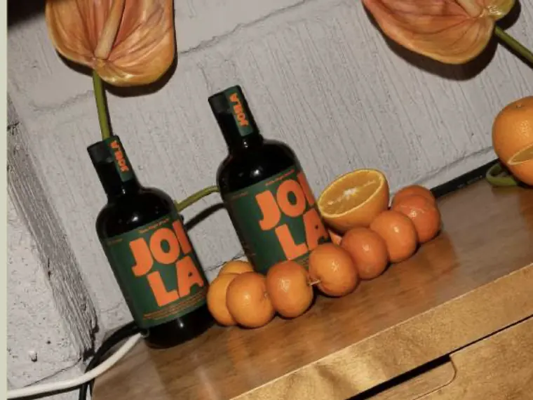 JOLA olive oil bottles styled with oranges and anthurium flowers on a wooden counter