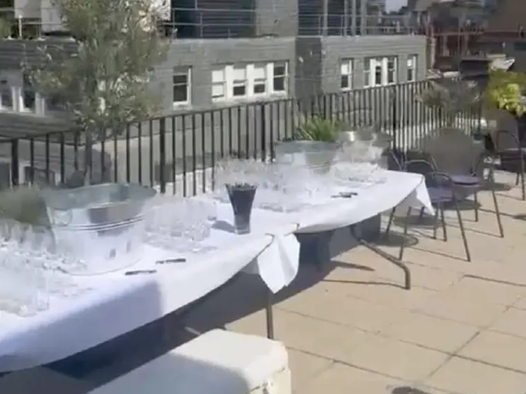 Rooftop table dressed in white linen with glassware and planting, overlooking the London skyline