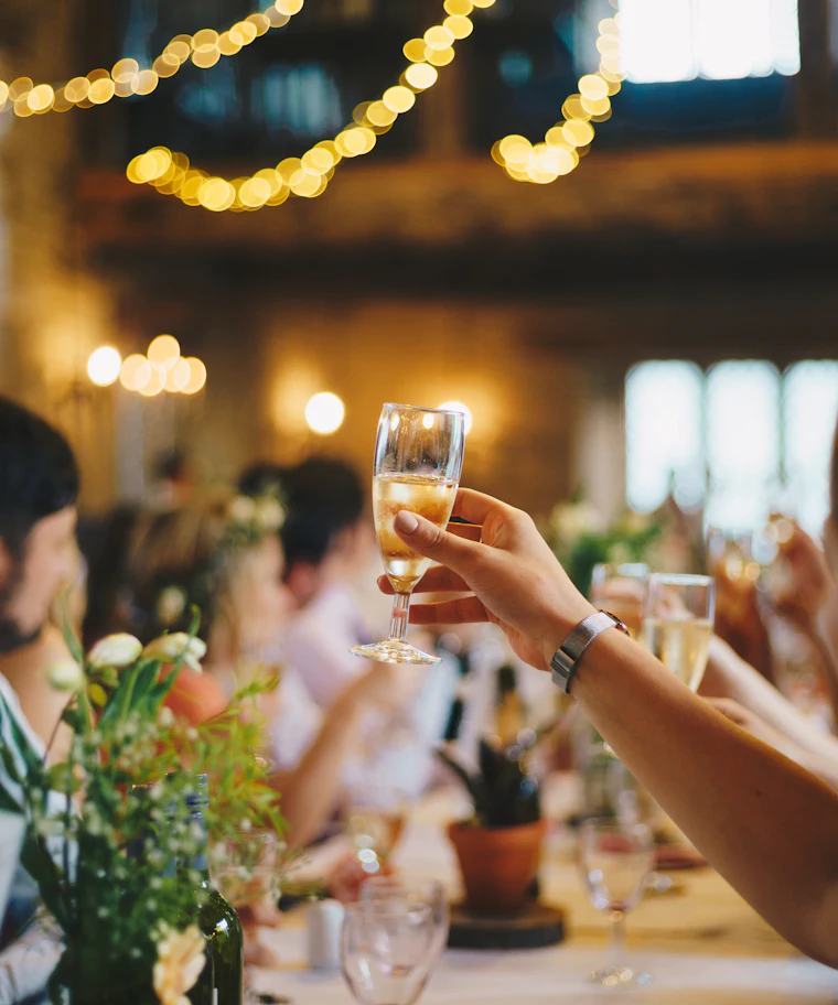 Guests raising a toast at a styled party table with bud-vase florals under warm string lights